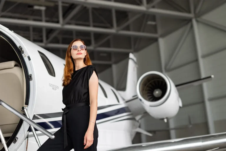 Eine selbstbewusste Frau in schwarzer Kleidung und mit Sonnenbrille steht neben einem Cessna Citation XLS Jet in einem Hangar, der den Luxus und den Lebensstil eines Owner Clubs repräsentiert.